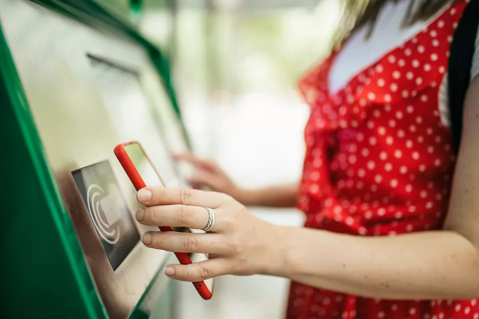 Close-up of woman holding up smartphone up to contactless public transit payment kiosk